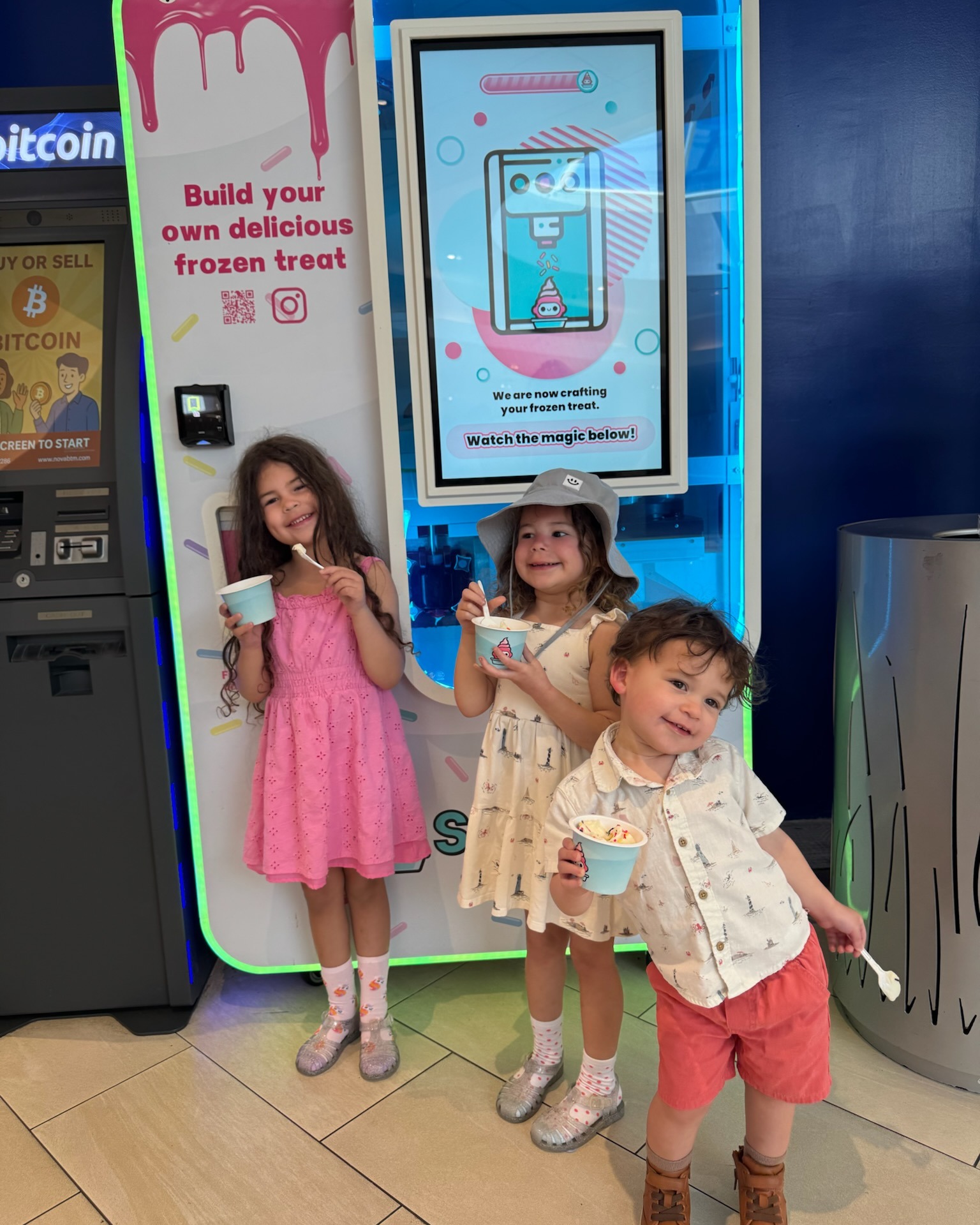 Three kids smiling with 99 Spoons cups in front of the kiosk